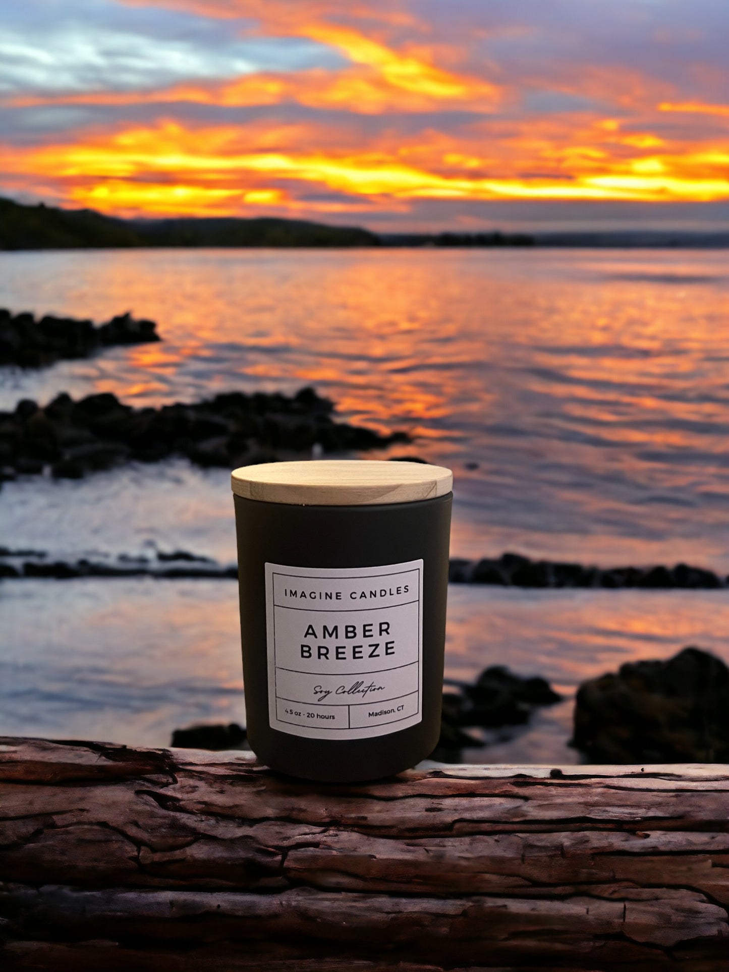 A candle in a glass jar sits on a wooden surface. The label reads 'Amber Breeze', evoking the final moments of Indian summer transitioning into autumn. The fragrance notes include ozone, citrus, sandalwood, benzoin, dark musk, cedar, amber, and powder. Infused with natural essential oils like cedar, patchouli, and clove leaf.