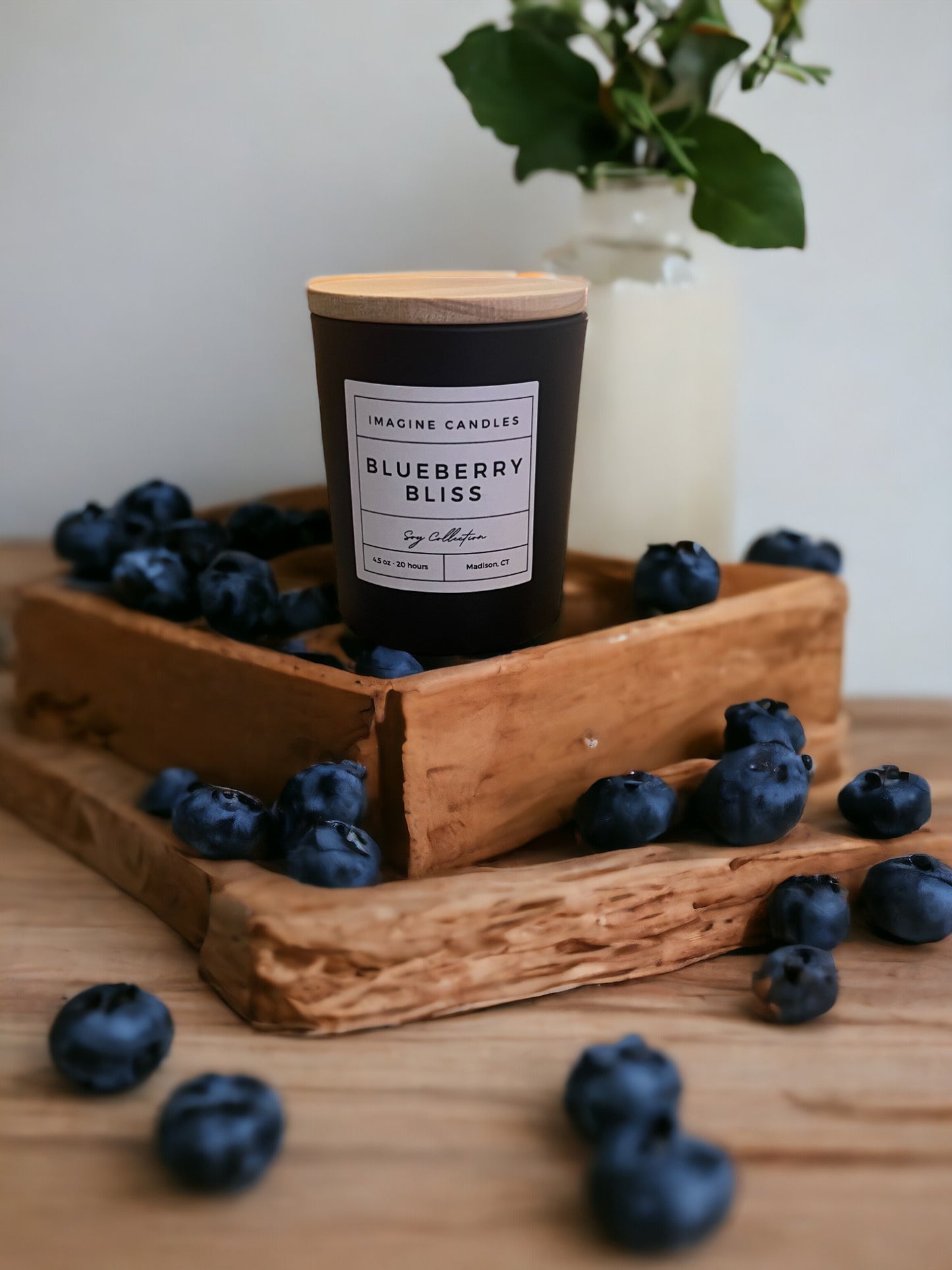 A Blueberry Bliss candle sits on a wooden counter next to fresh blueberries, embodying the essence of indulgence. Fragrance notes include butter, sugar, blueberry, graham cracker, and vanilla, reminiscent of a once-a-year blueberry pie from the local farmer’s market.