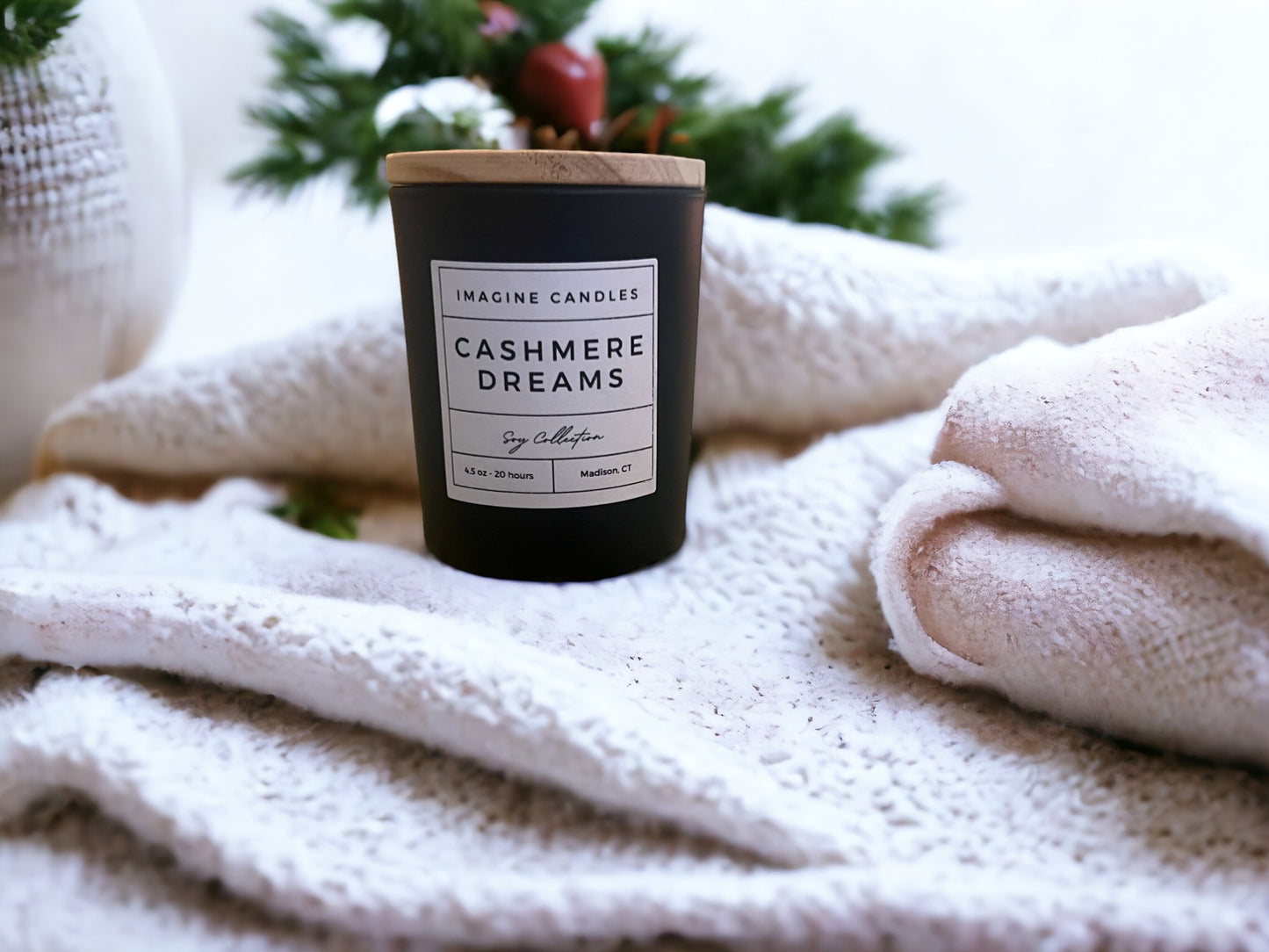 A candle rests atop a stack of neatly folded towels. The label reads 'Cashmere Dreams', evoking the sensation of comfort and relaxation. The fragrance notes include bergamot, saffron, violet, amber, lily of the valley, dark musk, vetiver, and powder.