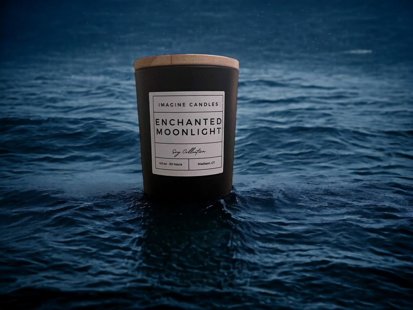 A candle rests overlooking moonlit water. The label reads 'Enchanted Moonlight', evoking the serene ambiance of a starry night. The fragrance notes include bergamot, citrus, green, aromatic, spice, herbal, cedarwood, and sandalwood