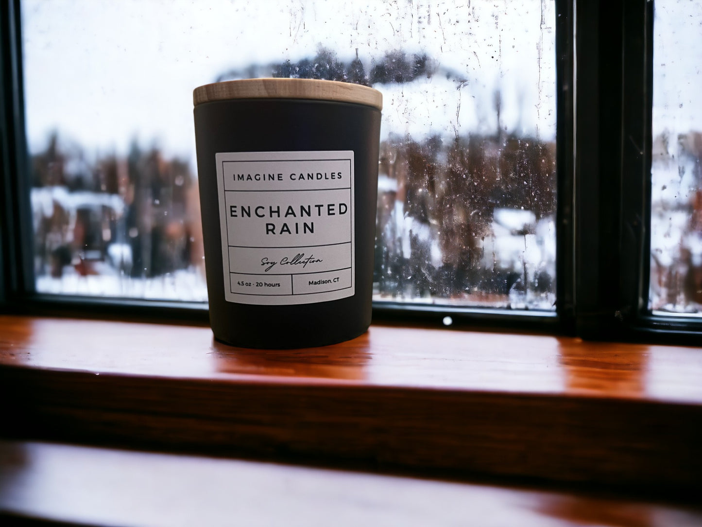 A candle sits on a rainy windowsill, evoking the ambiance of the first rainfall of Spring. The label reads 'Enchanted Rain', capturing the essence of the purifying rain. The fragrance notes include green leaves, lily of the valley, rose, ozone, and sandalwood. Infused with natural essential oils, including orange peel, lemon peel, and petitgrain leaf