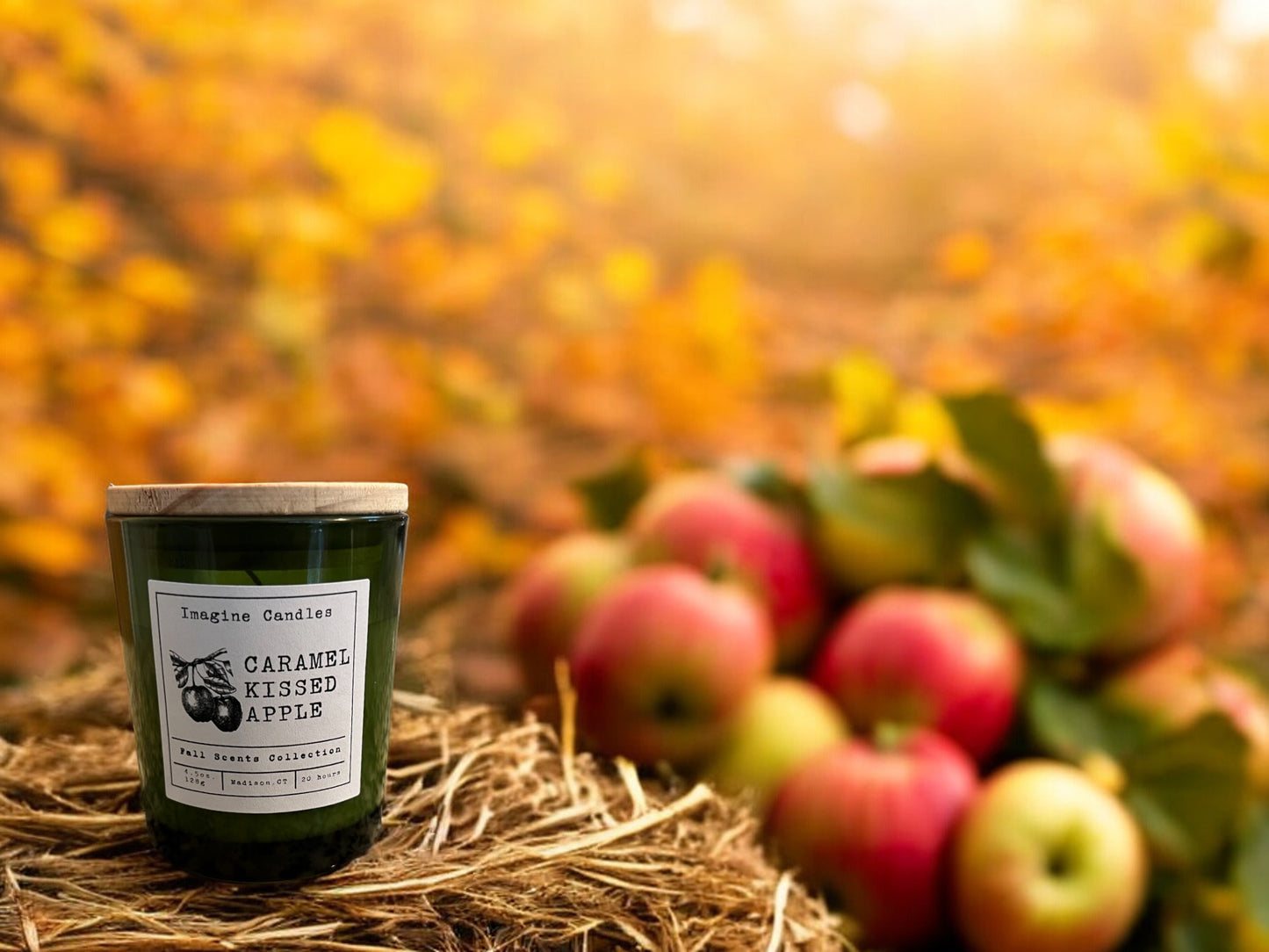 A green candle jar sits on a hay bale with two apples in the trees in the background are changing colors