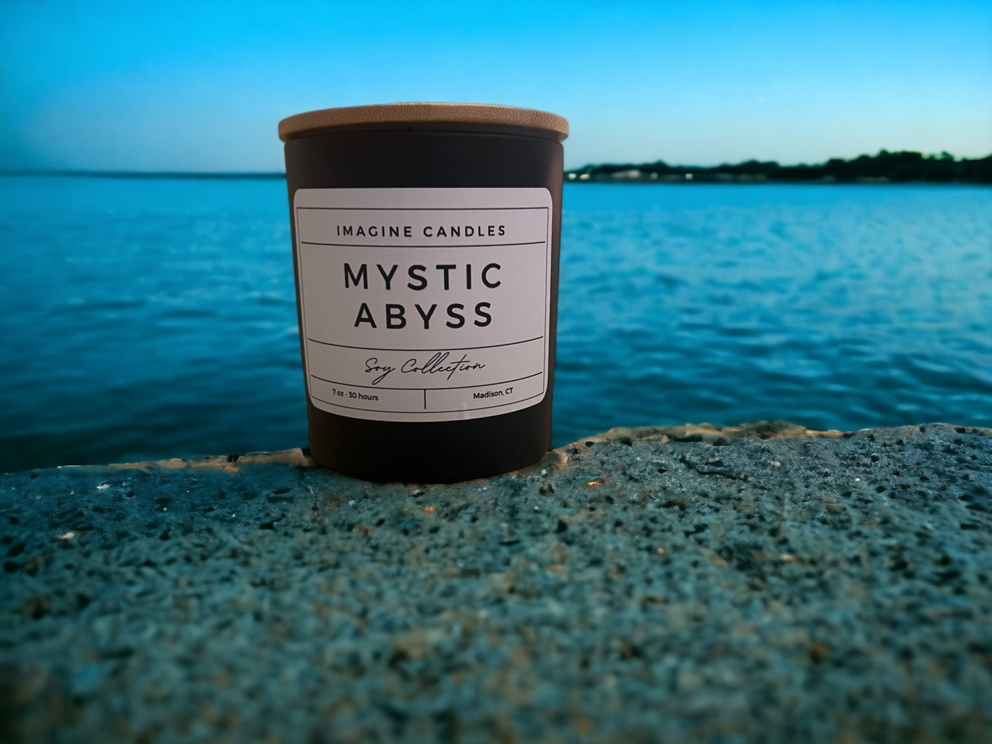 A candle sits along the shore, embodying the essence of Mystic Abyss. The label reads 'Mystic Abyss', evoking a sense of solitude and contemplation. The fragrance notes include petitgrain, ozone, sea salt, plum, eucalyptus, dark musk, sandalwood, and powder. Infused with natural essential oils, including sweet orange, mandarin, cinnamon bark, clove leaf, clove bud, pine, grapefruit, mentha leaf, cumin, and wheatgerm."