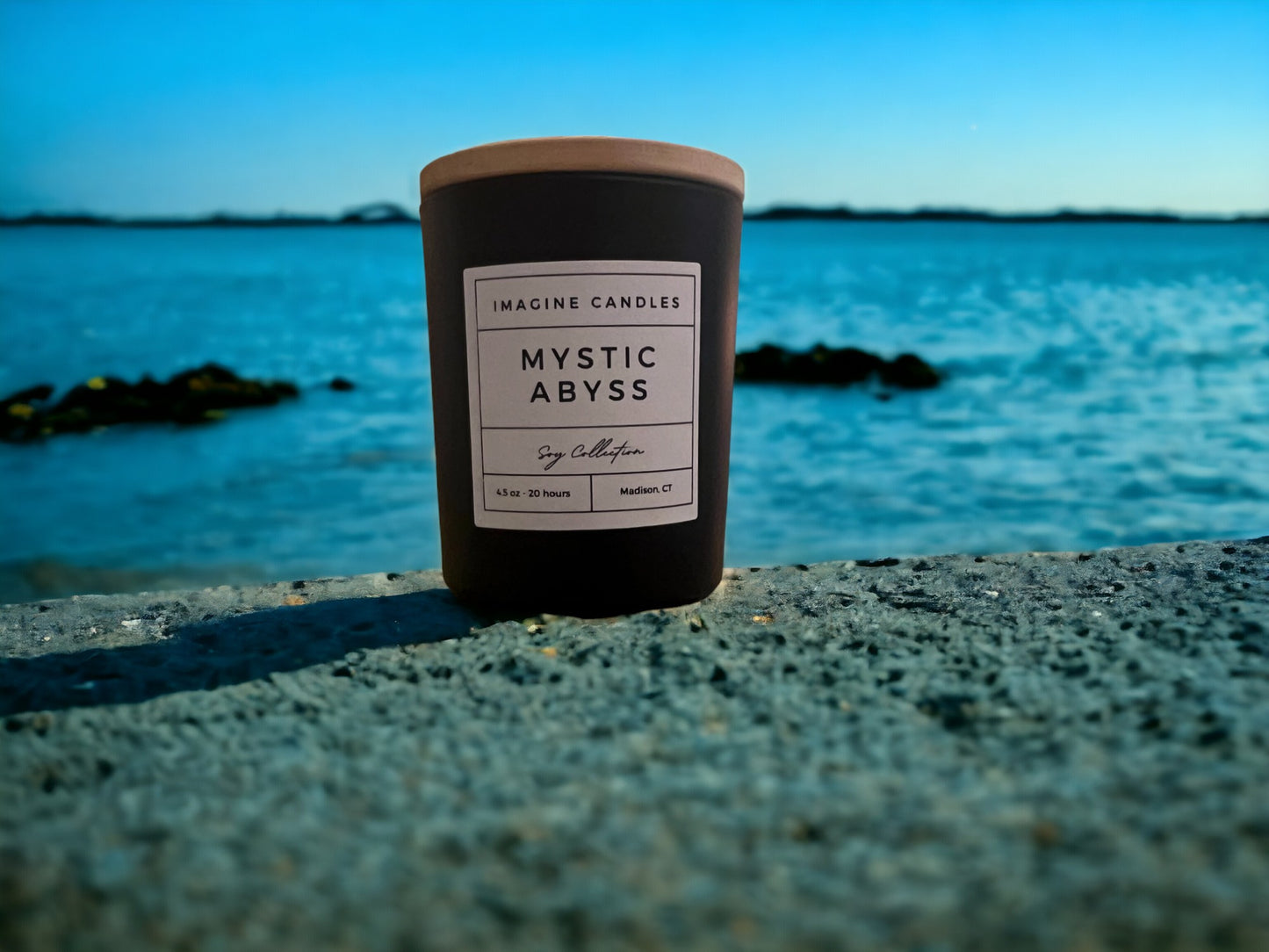 A candle sits along the shore, embodying the essence of Mystic Abyss. The label reads 'Mystic Abyss', evoking a sense of solitude and contemplation. The fragrance notes include petitgrain, ozone, sea salt, plum, eucalyptus, dark musk, sandalwood, and powder. Infused with natural essential oils, including sweet orange, mandarin, cinnamon bark, clove leaf, clove bud, pine, grapefruit, mentha leaf, cumin, and wheatgerm."