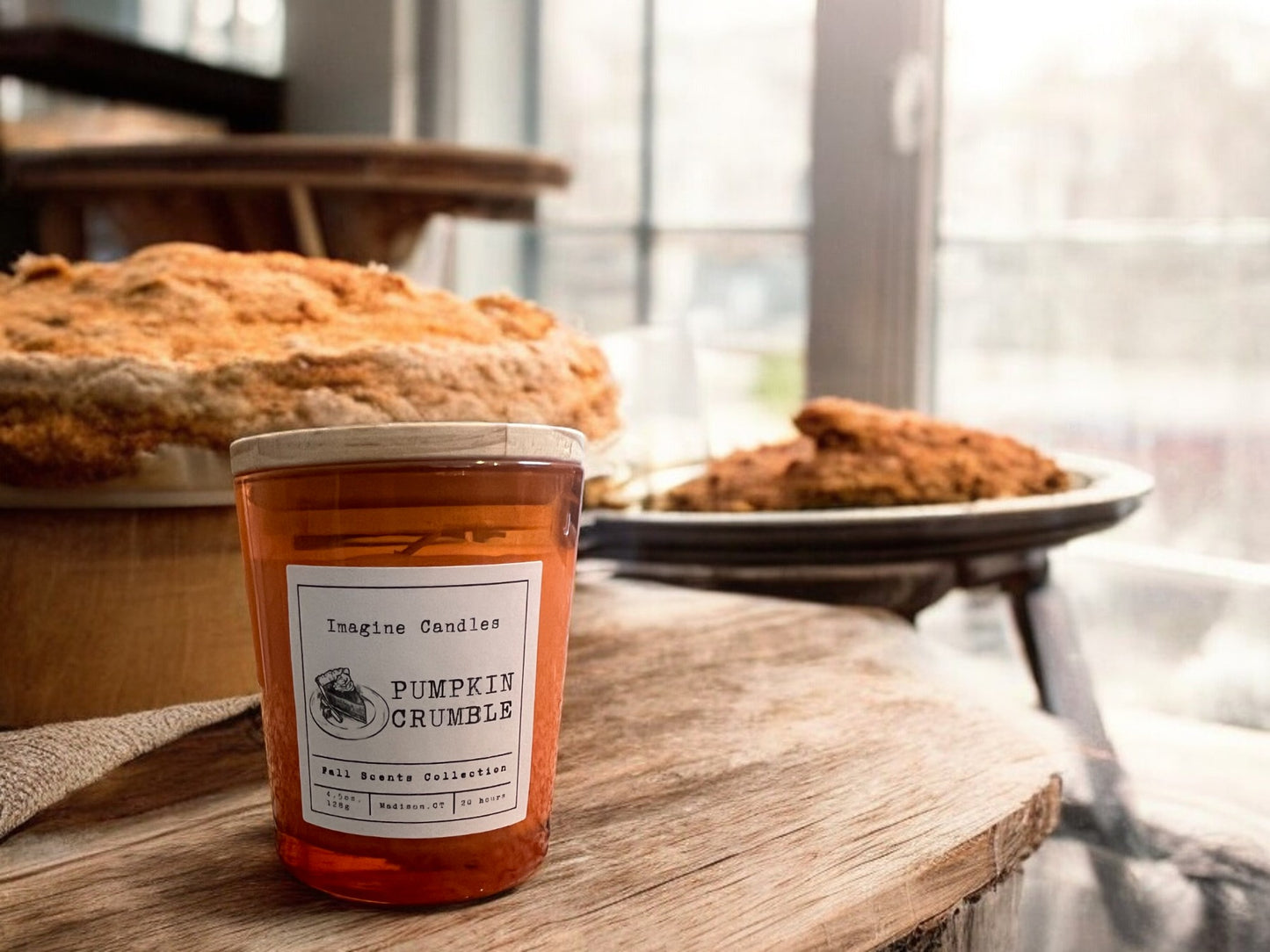 A Pumpkin Crumble candle on a bakery counter next to a pumpkin pie, evoking the warm, spicy aroma of a freshly baked pumpkin dessert with a buttery crumble topping.