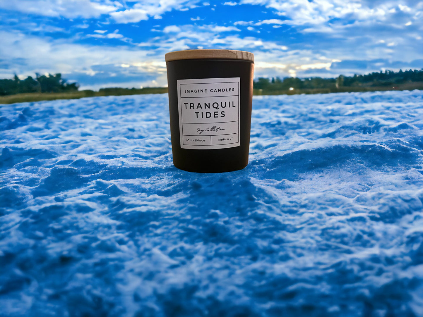 A candle rests on blue ocean waves, embodying the essence of Tranquil Tides. The label reads 'Tranquil Tides', evoking the feeling of the first day of a beach vacation, relaxing by an open window. Fragrance notes include bergamot, sea salt, peony, mint, juniper, light musk, and marine, infused with natural essential oils, including lemon, peppermint, and lime.