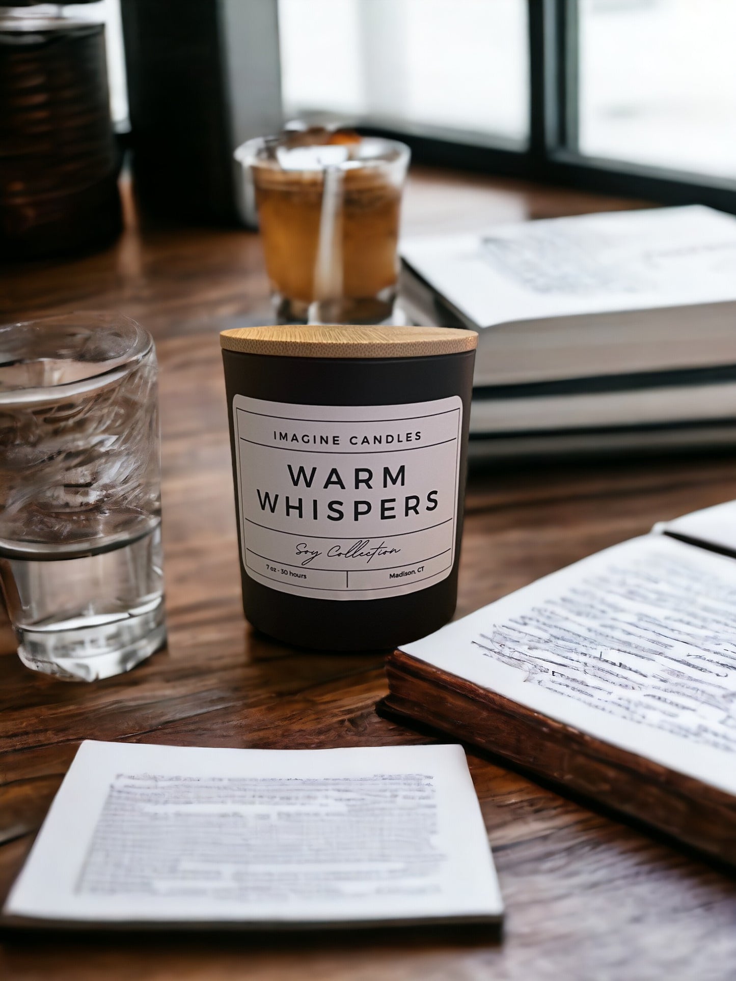 A candle sits on a table with a drink and a book, embodying the essence of Warm Whispers. The label reads 'Warm Whispers', evoking the feeling of excitement and energy. Fragrance notes include petitgrain, orange, grapefruit, cotton blossom, coconut, musk, powder, and wood, infused with natural essential oils, including orange peel, juniper, grapefruit peel, lemon peel, and tangerine."