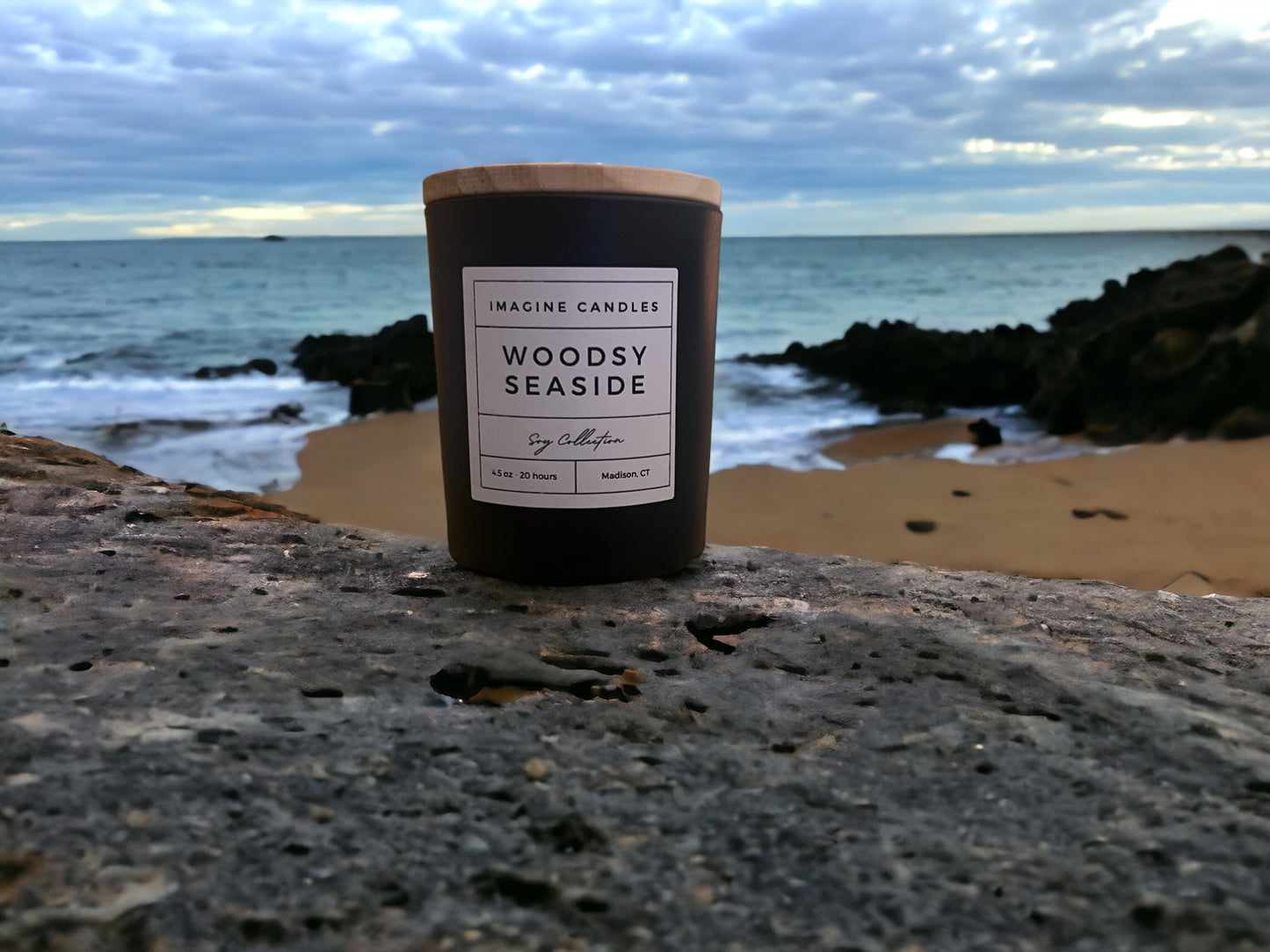 A candle rests at the edge of the woods and beach, epitomizing the essence of Woodsy Seaside. The label reads 'Woodsy Seaside', evoking the symbiosis of yin and yang where forest meets ocean. Fragrance notes include sea salt, orange peel, grass, eucalyptus, sage, marine, patchouli, teakwood, and moss, infused with natural essential oils, including patchouli, cedarwood, clove leaf, elemi, eucalyptus, orange sweet, guaiacwood, cedar, pine, clary sage, and galbanum