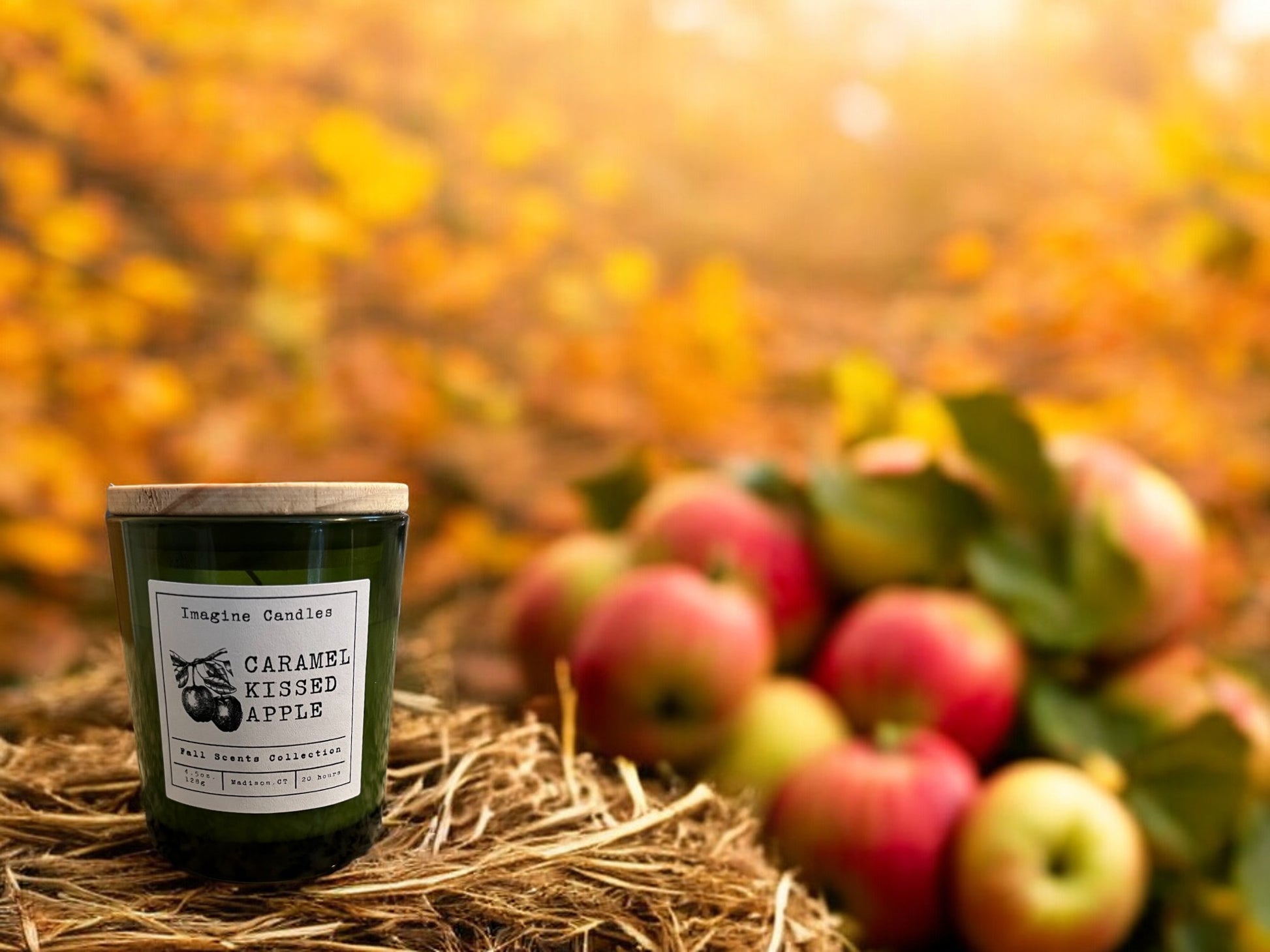 A green candle jar sits on a hay bale with two apples in the trees in the background are changing colors
