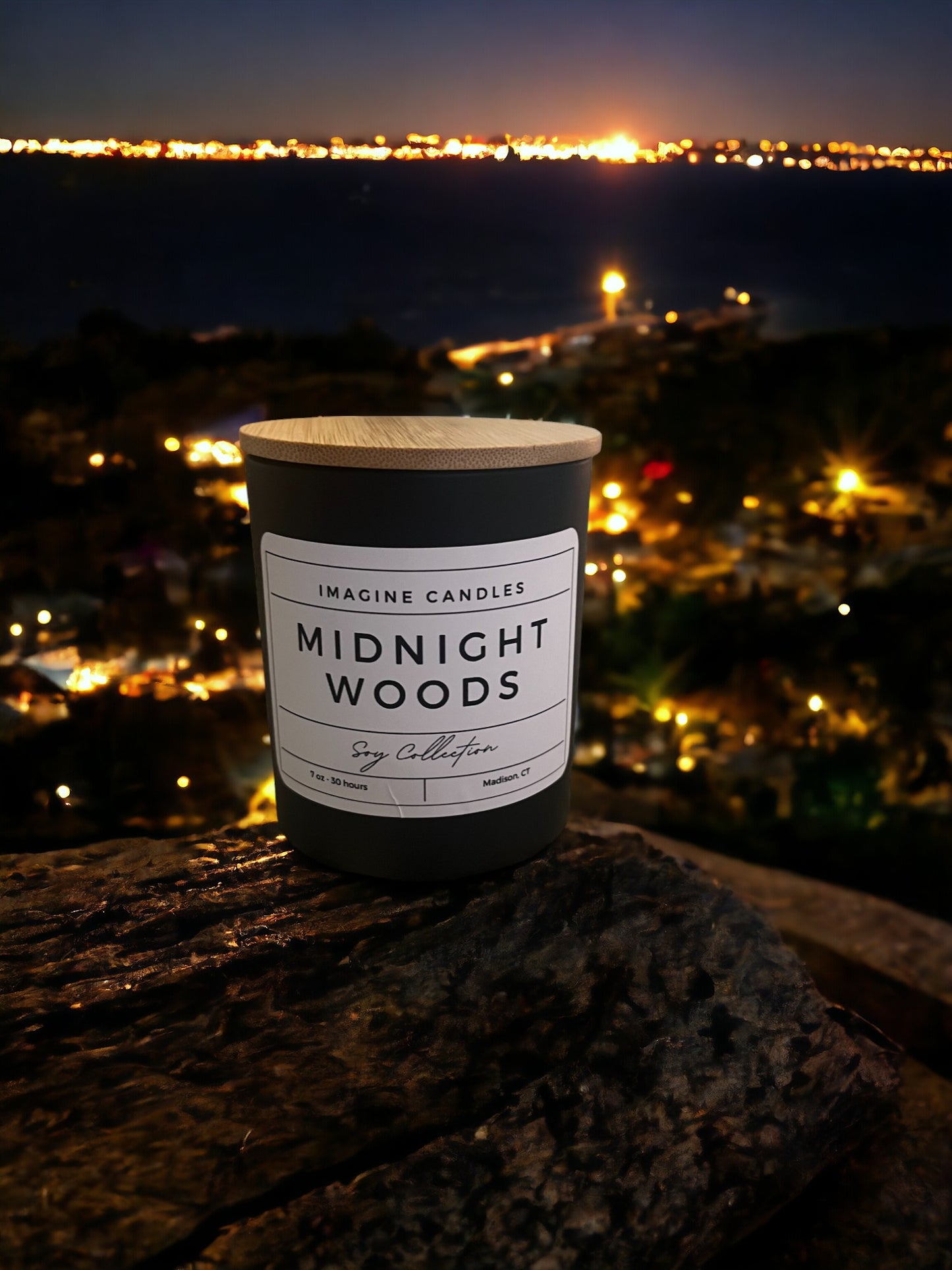 A candle overlooks a skyline at night, embodying the essence of Midnight Woods. The label reads 'Midnight Woods', evoking the feeling of staying up late watching an investigative thriller. The fragrance notes include citrus, plum, amber, jasmine, dark musk, amyris, and benzoin. Infused with natural essential oils, including cypress, cedarwood, patchouli, mandarine/tangerine, sweet orange, nootka tree, and davana