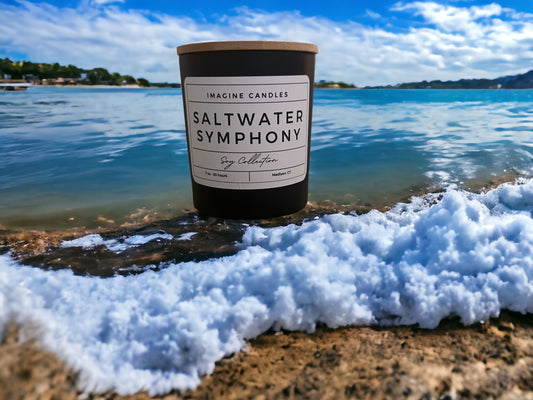 A candle sits along waves breaking on the shore, embodying the essence of Saltwater Symphony. The label reads 'Saltwater Symphony', evoking the sensation of water composing music and invigorating mind, body, and spirit. Fragrance notes include cardamom, orange peel, sea salt, light musk, palm, and amber, infused with natural essential oils, including cardamom, clove, and orange